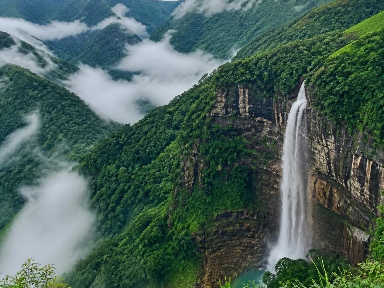 a realistic scenic photo of meghalaya with lush green hills, misty valleys, a waterfall, and a bright natural landscape